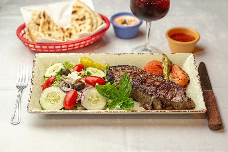 Rib eye steak entree with salad topped with cucumbers and cherry tomatoes